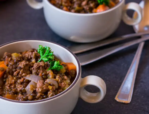 fresh cooked spicy stew with minced meat and legumes served in bowls with spoons on a table