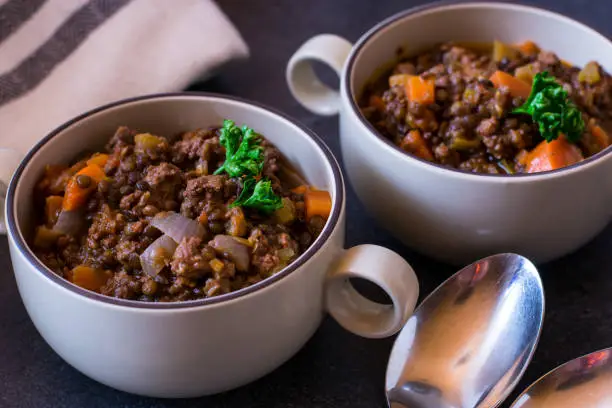 fresh cooked minced meat stew with legumes and vegetables served in soup cups on a table with spoon