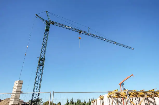 Photo of Huge construction crane and a smaller crane on a construction site with fence in the foreground and a lot of blue sky - plenty of copyspace