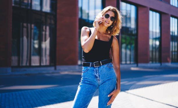 istock Confident young lady in jeans and sunglasses using smartphone on street 1301948531