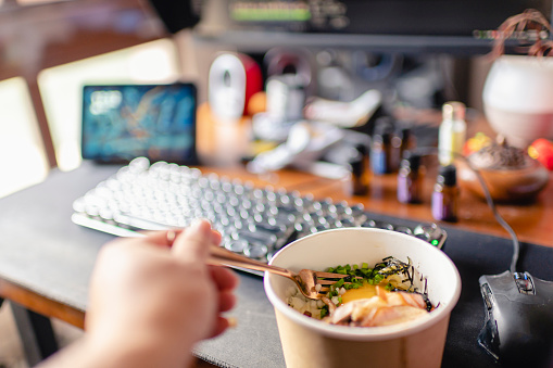 first person view with a paper bowl of ramen with egg york and char siu in front of desktop pc