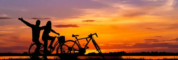 Silhouette Couple cycling on sunrise background.Gorgeous Panorama twilight sky and cloud at morning background image.