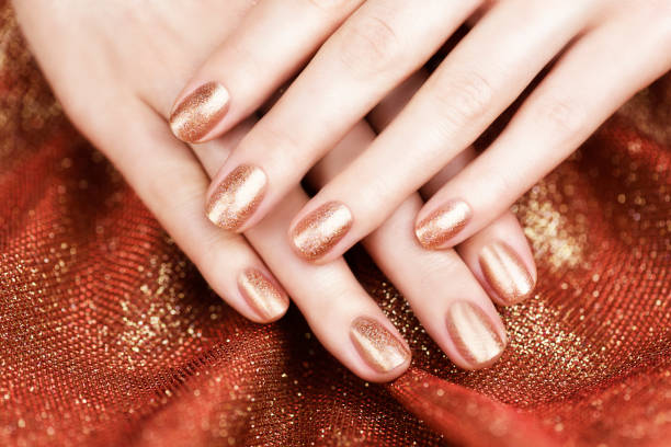 istock Female hands with bronze-colored manicure on a shiny bronze background. Bronze manicure. 1301951351