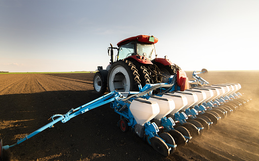 Farmer with tractor seeding - sowing crops at agricultural field. Plants, wheat.