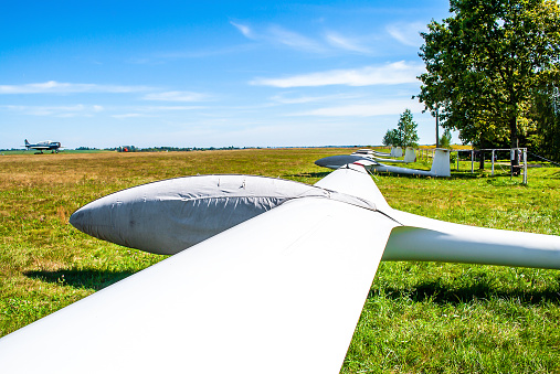 Old glider parked in protection covers standing in summer field by blue sky, selective focus