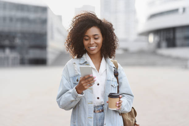 joven usando teléfono inteligente en una calle de la ciudad - portrait women laughing black fotografías e imágenes de stock