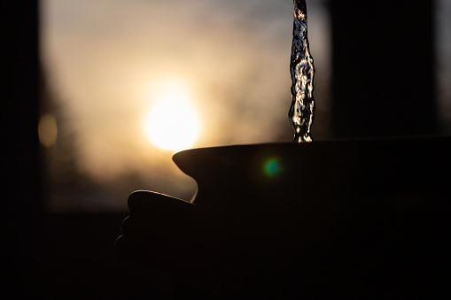 Silhouette of water pouring into clay pot