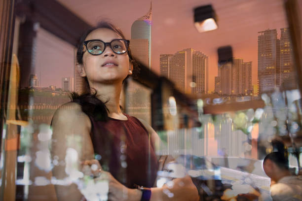 donna asiatica all'interno di un ufficio con giacarta cityscape riflessione in finestra - reflection women contemplation ethnic foto e immagini stock