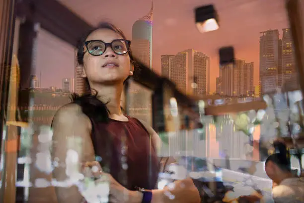 asian woman inside a office with reflection  of Jakarta Cityscape, capital city of Indonesia  in window