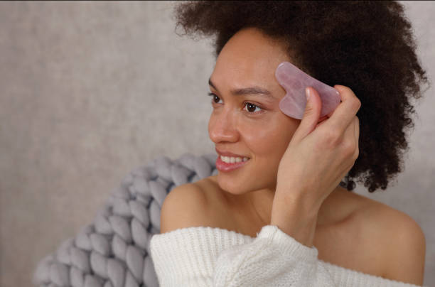 masaje gua sha cara con piedra de jade. tratamiento de elevación y antienvejecimiento. enfoque seloctivo en el masajeador - spooning fotografías e imágenes de stock