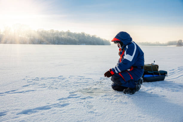 un pêcheur pêche avec une canne de filature d’hiver sur un lac gelé. concert de pêche sur glace. - ice fishing photos et images de collection