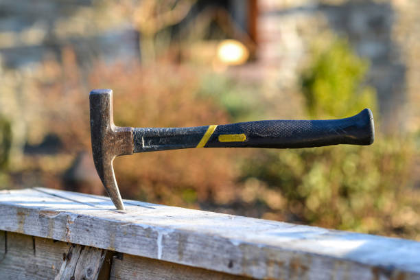 Concept manual work or craftmanship: Well used hammer stucks in a wooden workbench outdoors - selective focus, little depth of field, lot of copy space Well used scabbling pick, hammer, stucks in a wooden workbench outdoors in the evening sun, work break, stop or break or finish construction lunch break stock pictures, royalty-free photos & images