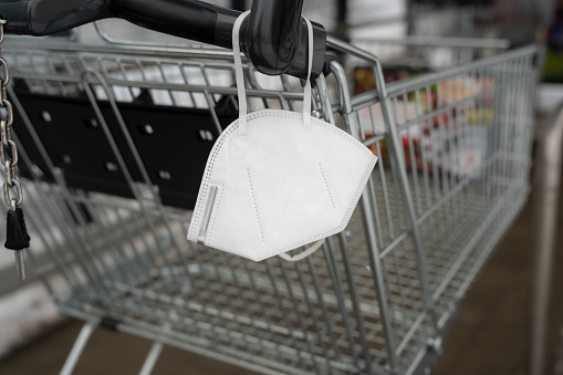 FFP2 face mask on a shopping cart of a retail store. Disposable white Covid-19 protection in a public place to prevent an infection. Pandemic measures.