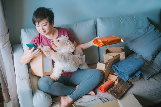 アジアの中国の中年の成人女性は喜んですべてのパッケージを開いて開く開き、彼女の購入したすべての彼女の購入したリビングルームのソファで配達されたオンラインショッピングからす� - dog pets stroking women ストックフォトと画像