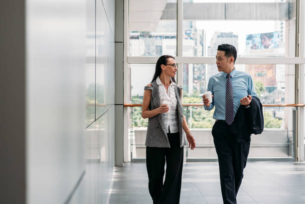 istock Two colleagues walking and talking in office hall 1301970609