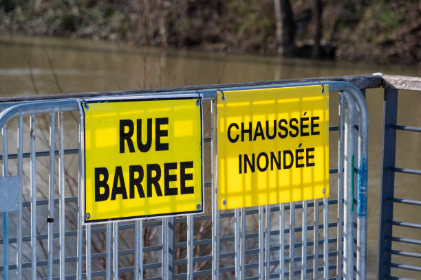 Two yellow warning signs fixed on a metal fence and written in French: "Closed street" and "Flooded pavement" Weather - Flood warnings in France. Two yellow warning signs fixed on a metal fence and written in French: "Closed street" and "Flooded pavement". The river Seine is visible in the background pavement ends sign stock pictures, royalty-free photos & images