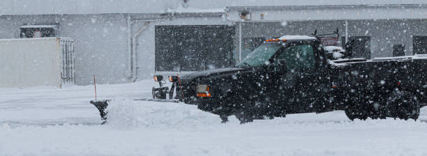 vista lateral del camión negro con un arado quitando nieve del estacionamiento durante la tormenta - snowplow snow parking lot truck fotografías e imágenes de stock