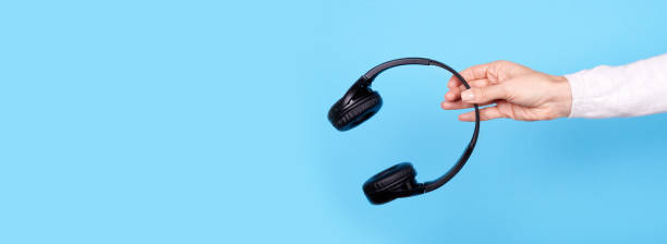 istock Hand with black wireless headphones on blue background. 1301988155