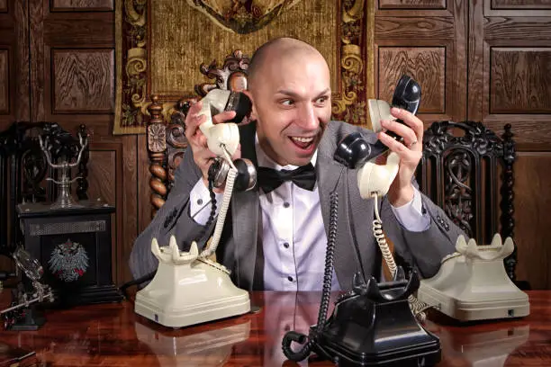 Fast-paced desperate businessman showman works in office and many calls, he keeps lot handsets. Business management concept. Stressed man talks on many phones at once. Copyright space