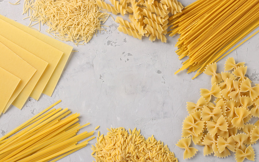 Border of raw pasta durum wheat on gray. Flatlay style.