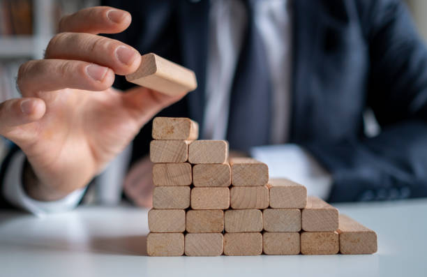 istock Businessman hand pulling out or placing wood block on the tower and semi-pyramid in modern office. Plan and strategy in business. 1301990457