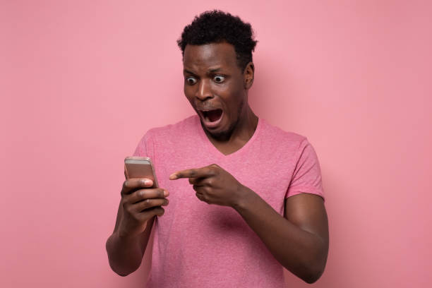 istock Young african man recieves message reminder on smart phone in bewilderment. 1301991529