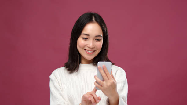 istock Young asian woman use phone and laugh against marsala copyspace 1301995486