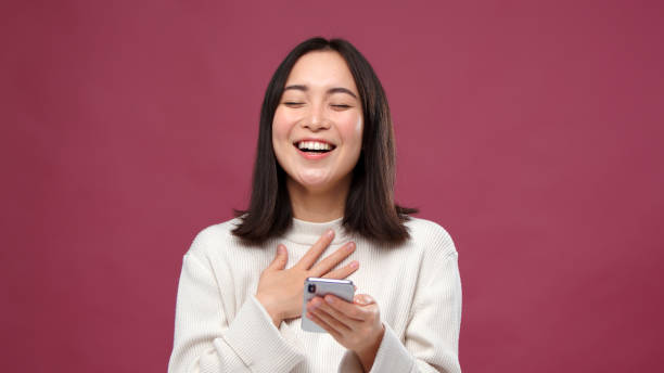 istock Young asian woman use phone and laugh against marsala copyspace 1301995523