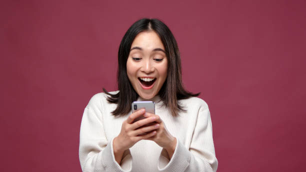 istock Young asian woman surprised with phone against marsala copyspace 1301995532