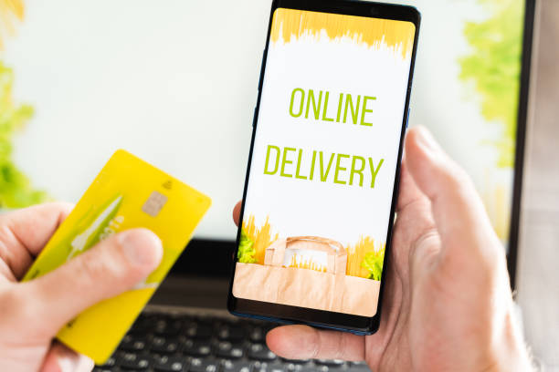 istock Hand with mobile phone. Online internet shopping, order through mobile application. Laptop. Home delivery of food, groceries from grocery store. Paper bag with pasta on screen. Payment by credit card 1301995539