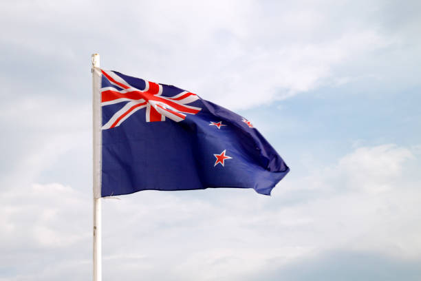 istock New Zealand flag on blue sky with clouds background 1301996424