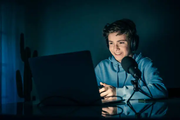 Young blogger and video game streamer playing at home with laptop. Vlogger filming himself having fun using technology to connect with audiences.Teenager play with online friends using gaming console.