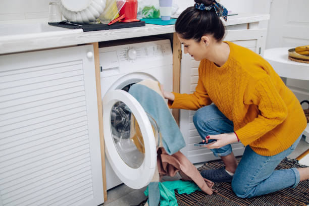 istock Young woman putting laundry for washing and using a smartphone 1302001833