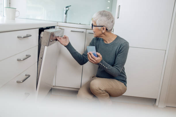 donna matura che guarda un tutorial per la gestione di una lavastoviglie - manual handling foto e immagini stock