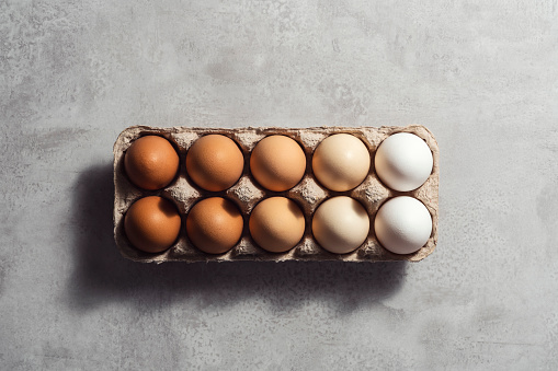 Box of color gradient brown eggs, rectangular egg carton on grey background. Easter eggs. Shot from directly above.
