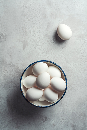 White eggs in an enamel bowl on gray rustic background. Shot from directly above.