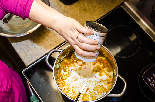 Woman pouring coconut milk in pan over the stove to make a vegan soup