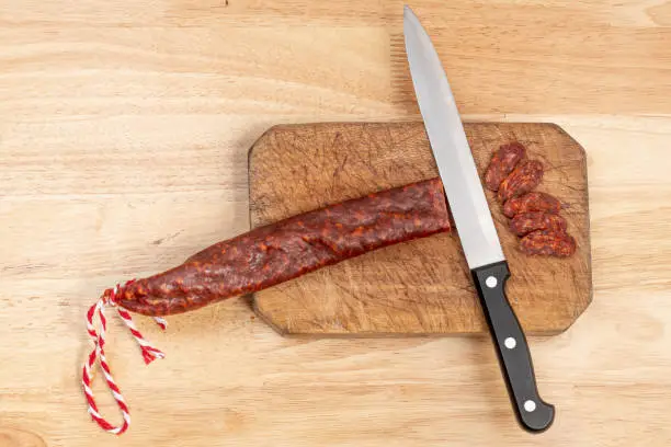 Photo of Sausage cut on wooden plank with knife