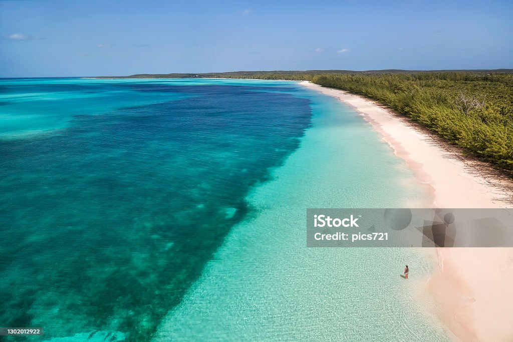 Aerial View on Cat Island Aerial view of a woman standing along the shoreline and enjoying the views of the turquoise waters and a brilliant pink beach in Cat Island, Bahamas Bahamas Stock Photo