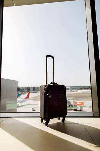 Small black suitcase with the handle extended standing next to an airport window