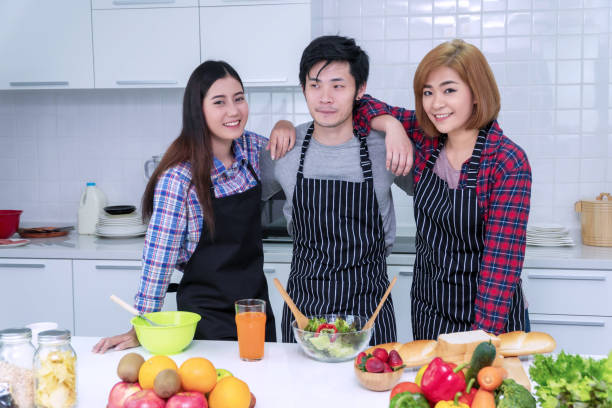 istock Friendship concept. Group young friends standing in kitchen with table learning cook healthy food together. Enjoying young man and woman holding hands on shoulder together while having celebration. 1302035627