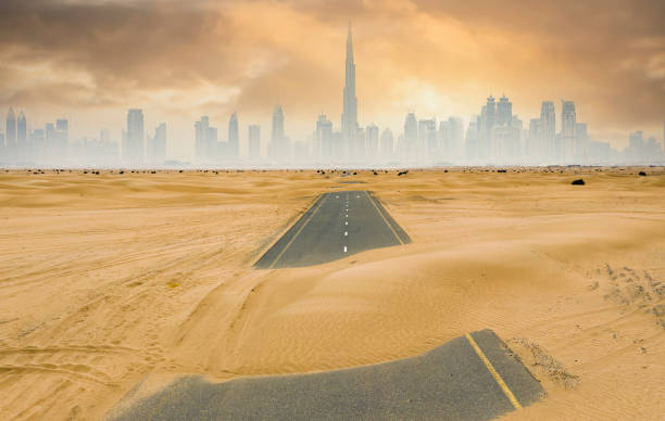 blick von oben, atemberaubende luftaufnahme einer einsamen straße, die von sanddünen bedeckt ist, mit der skyline von dubai im hintergrund. dubai, vereinigte arabische emirate. - fog desert arabia sunset stock-fotos und bilder