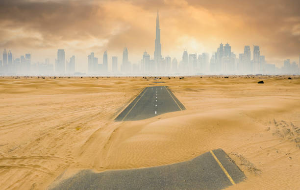 vista dall'alto, splendida vista aerea di una strada deserta coperta da dune di sabbia con lo skyline di dubai sullo sfondo. dubai, emirati arabi uniti. - fog desert arabia sunset foto e immagini stock