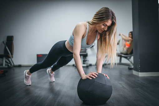 A fit young woman doing push ups with a medicine ball
