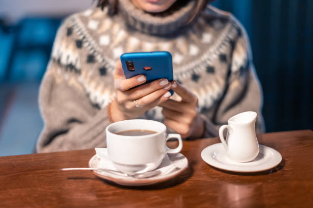 une jeune femme rédacteur ou blogueur travaille avec les réseaux sociaux sur son smartphone tout en s’asseyant dans un café et en sirotant du café chaud - coffee shop coffee break coffee cup holding photos et images de collection