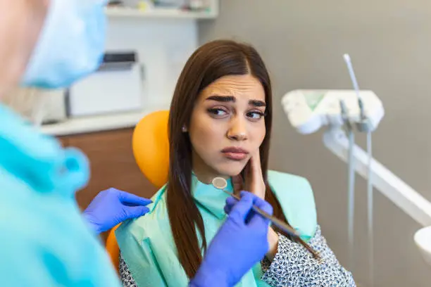 Young woman holding cheek in chair at dentist, having toothache. Shot of a young woman suffering from toothache while sitting in the dentist"u2019s chair