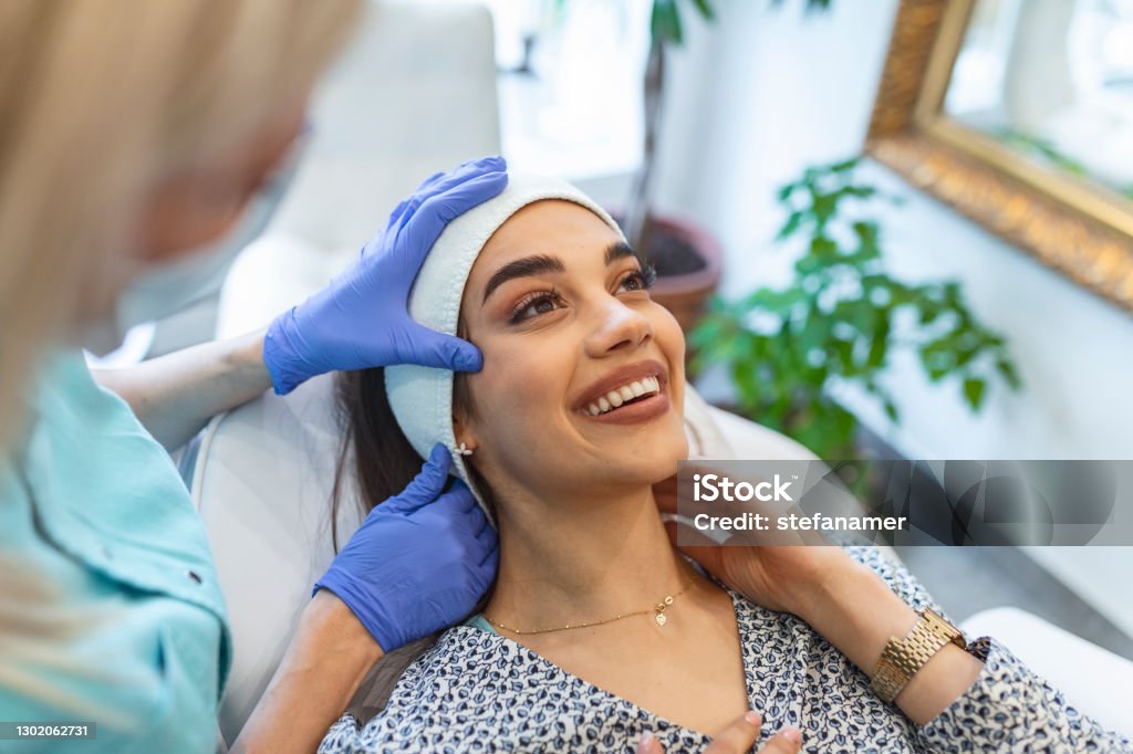 Masseur giving treatment to beautiful brunette. close-up, portrait of a young beautiful girl, with flawless skin, which the master masseur makes facial massage, in medical gloves. In a beauty salon Design Stock Photo