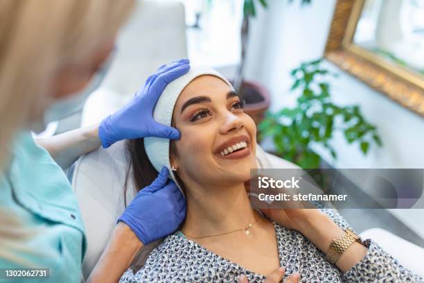 Masseur Giving Treatment To Beautiful Brunette Closeup Portrait Of A Young Beautiful Girl With Flawless Skin Which The Master Masseur Makes Facial Massage In Medical Gloves In A Beauty Salon Stock Photo - Download Image Now