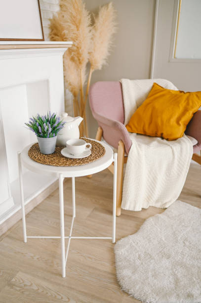 istock Stylish elegant eco composition living room with white breakfast table coffee cup teapot false fireplace dried flowers plants pampas grass pink powder armchair, blanket and pillow. Modern home decor 1302064583