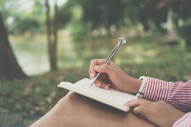 istock Woman hand writing down in small white memo notebook for take a note not to forget or to do list plan for future in public park. 1302068865